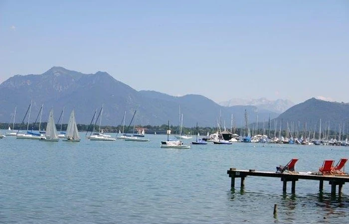 Vom Steg aus blicken Sie über den Chiemsee mit Segelbooten in die Chiemgauer Alpen.