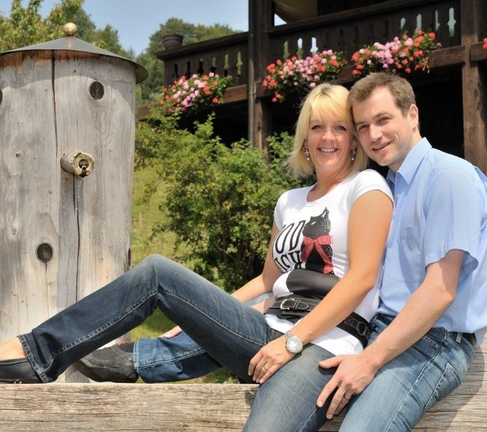 Auf einem Brunnen vor dem Berghotel Adersberg sitzen Ihre Gastgeber Herr und Frau Haase.