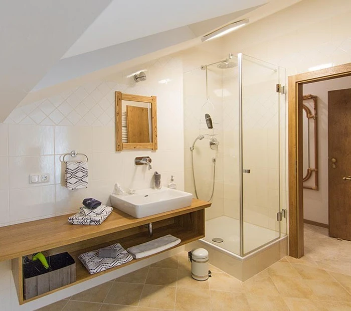 Das Bad in der Ferienwohnung ist modern in Holz und weiß gehalten. Zu sehen Waschtisch mit modernen Becken und Glasdusche.