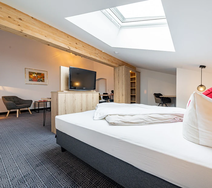 Eine Suite mit Doppelbett, Fernseher, Stühlen und Lampe im Berghotel Adersberg