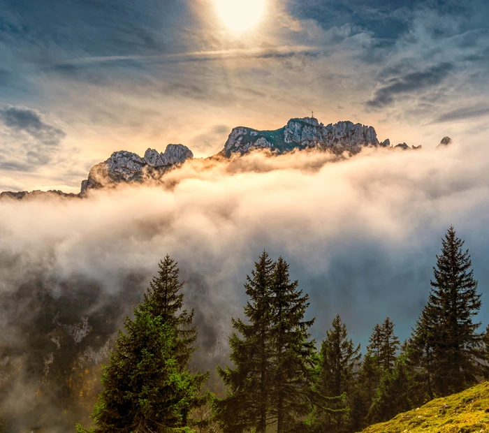 Blick auf die Kampenwand. Diese ist mit Wolken umhüllt und die Sonne scheint durch.