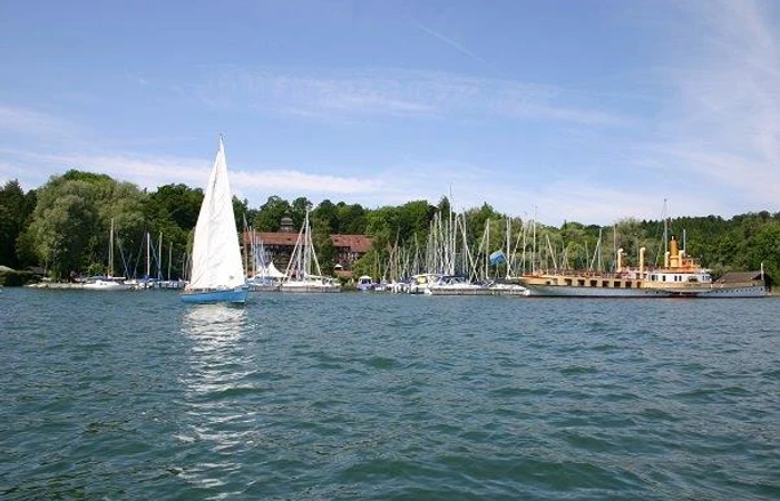 Blick vom Chiemsee aus auf das Yachthotel mit verschiedenen Segelbooten davor.