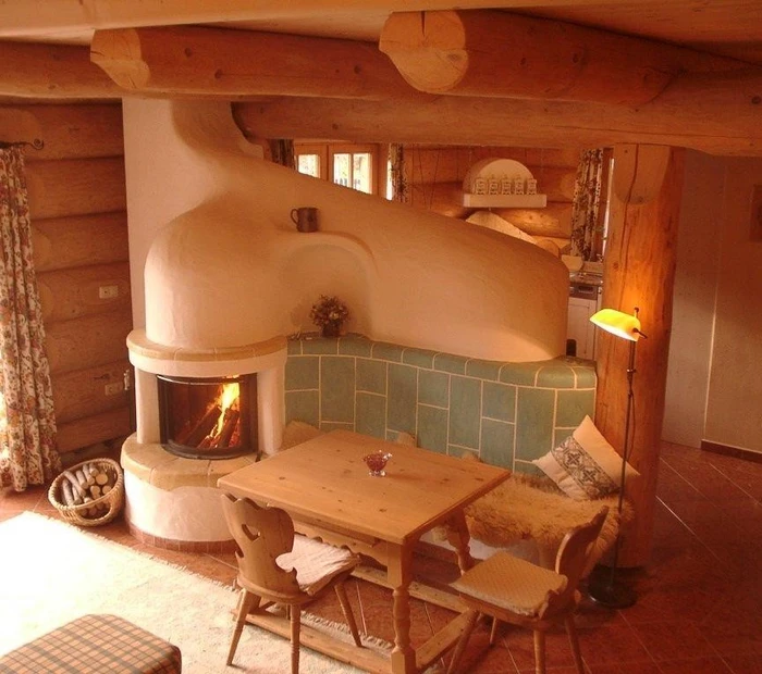 Kachelofen mit Ofenbank und Sitzgruppe im gemütlichen Naturstammhaus, Deckenbalken aus Stämmen