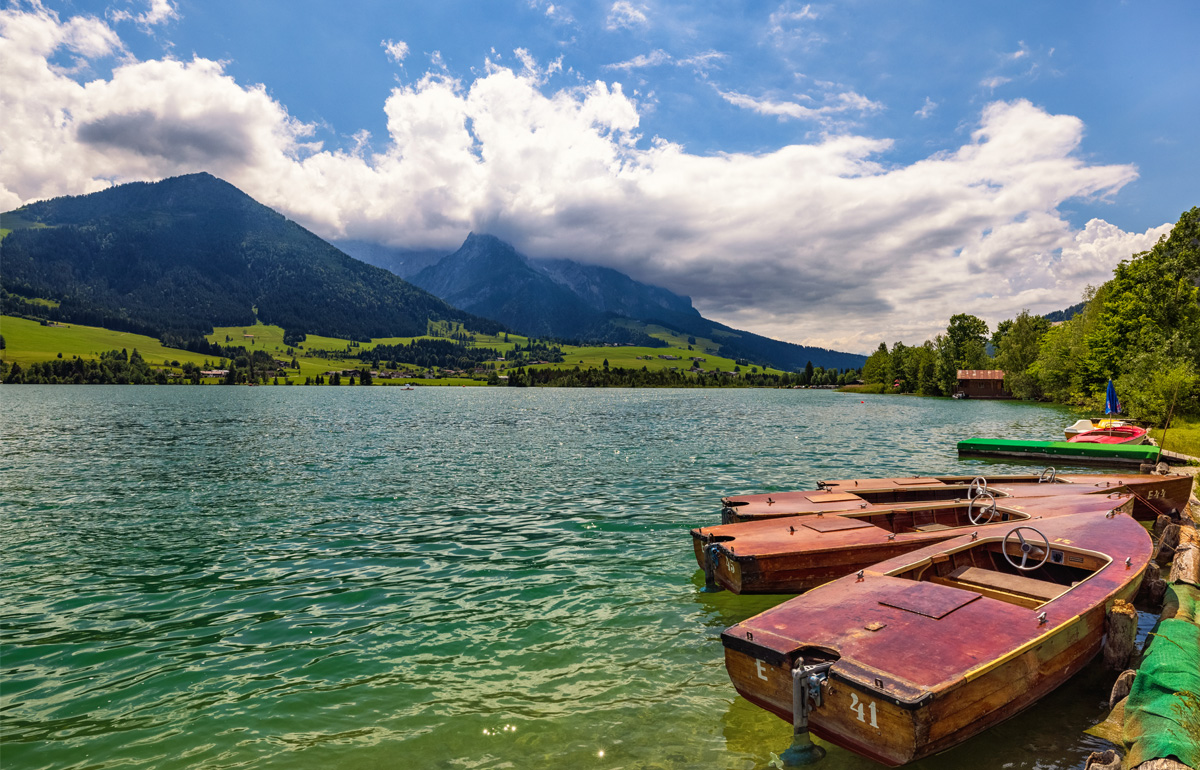 Auf dem Walschsee liegen kleine Boote im Hintergrund sehen Sie Berge.