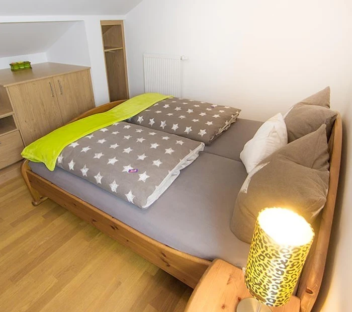 Das Schlazimmer in der Ferienwohnung Alpenblick ist in Holz, grau und weiß gehalten. Doppelbett, Nachtkästchen mit Stehlampe und kleine Schränke.