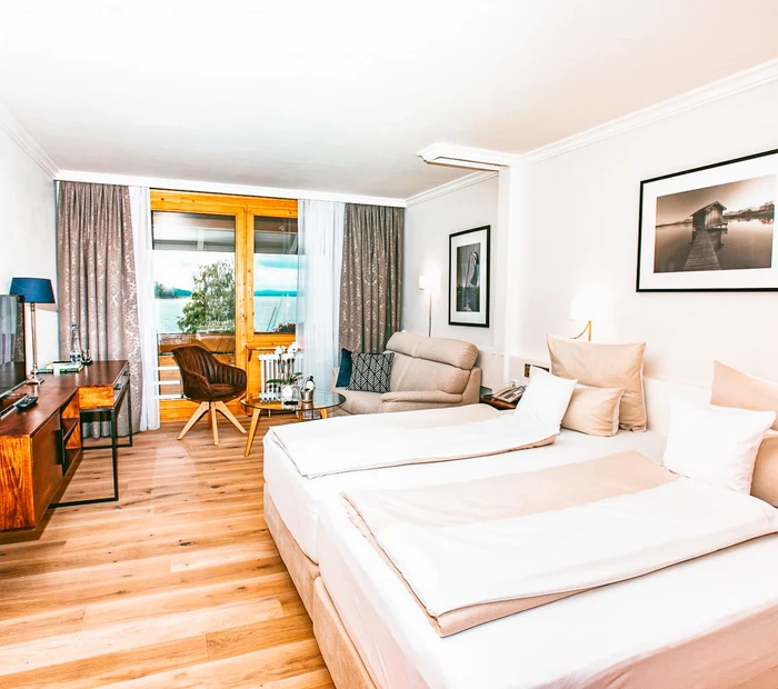 Das Superior Zimmer im Yachthotel Chiemsee ist in weiß, beige gehalten mit Holzboden und Blick auf den Chiemsee.