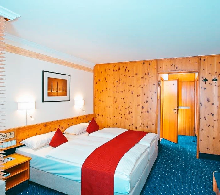 Zu sehen ist das Komfort Waldzimmer mit Doppelbett. Die Farben weiß, rot, blau , die Wände teilweise in Holz.