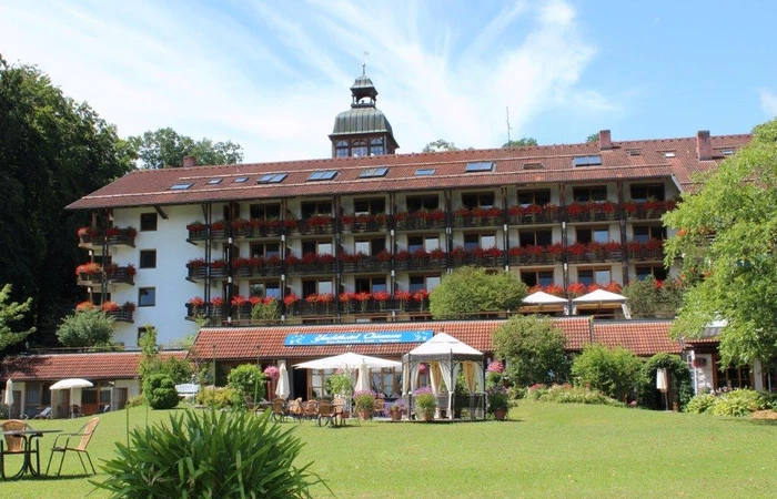 Sie stehen im Hotelgarten vom Yachthotel Chiemsee mit Blick in Richtung Hotelgebäude.