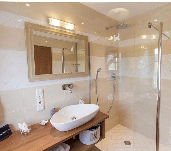 Das moderne Bad vom Deluxe-Zimmer mit Waschbecken, Spiegel, Glasdusche in Holz und weiß gehalten.